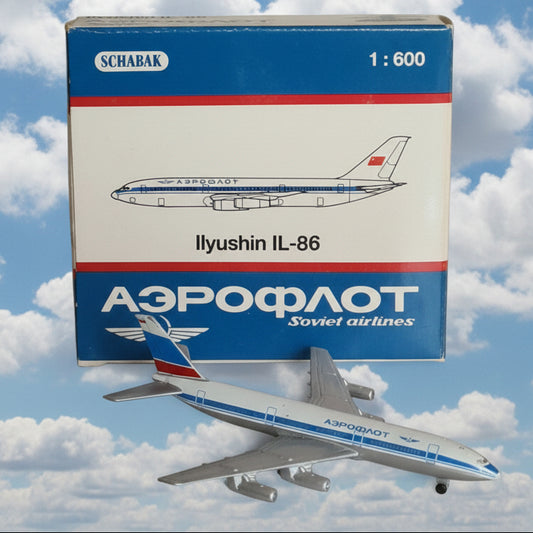 A 1:600 scale model airplane of an Ilyushin IL-86 passenger aircraft, shown next to its original blue and white Schabak box. The model features a white fuselage with blue and red stripes, matching the Soviet airlines livery depicted on the packaging.