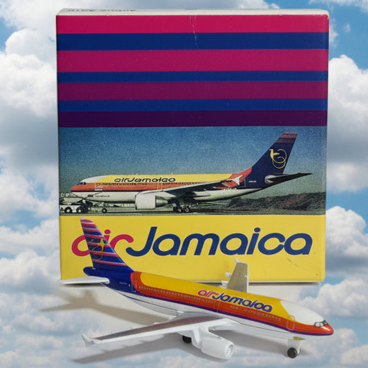 A small Air Jamaica model airplane placed beside its printed packaging box on a plain white surface. The box features vertical magenta and blue stripes on the left and a yellow side panel with the Air Jamaica name.