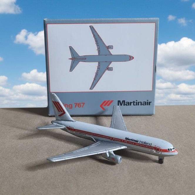 A small Martinair Boeing 767 model airplane placed beside its retail box on a plain tan cardboard background.
