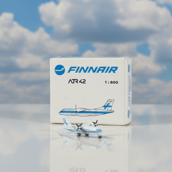 A small white and blue Finnair AR42 model airplane placed in front of its original white product box on a brown cardboard background.